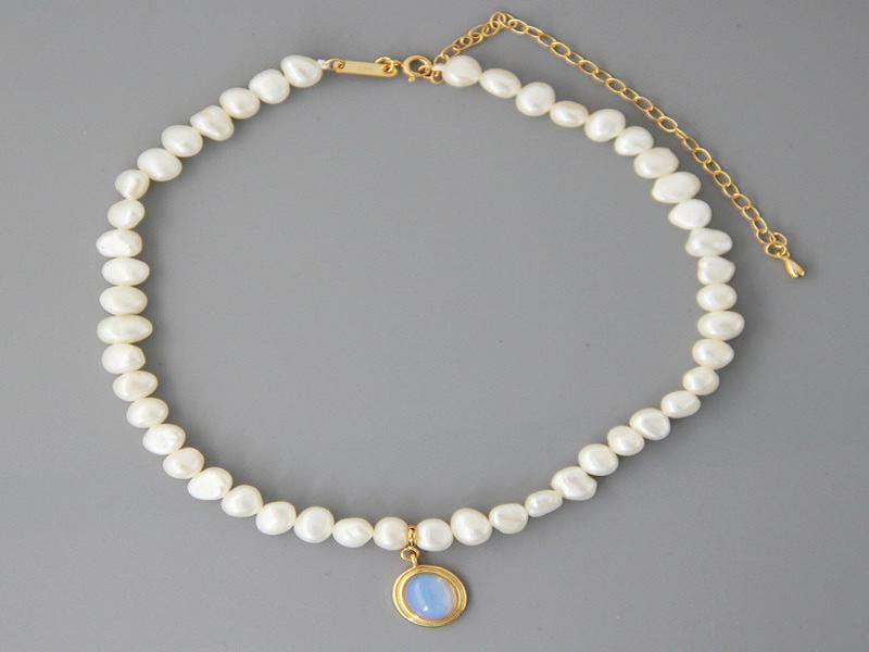 Perlenkette mit goldfarbenem Anhänger und blauem Schmuckstein auf grauem Hintergrund.